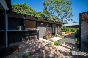 Backyard renovation with outdoor bar seating, modern walkway, and landscaped garden beds by Ground Up Builders