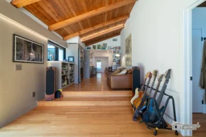Renovated living room with wooden ceiling, hardwood floors, and guitar collection by Ground Up Builders