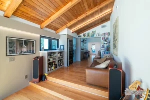 Renovated living room with wooden ceiling, bookshelves, and open layout by Ground Up Builders
