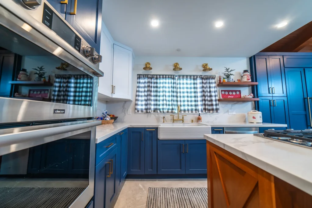 A kitchen corner featuring royal blue cabinets, white countertops, stainless steel appliances, and a plaid window curtain.