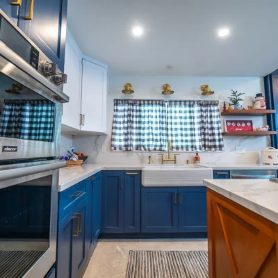 A kitchen corner featuring royal blue cabinets, white countertops, stainless steel appliances, and a plaid window curtain.