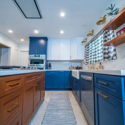 A spacious kitchen with blue lower cabinets, white upper cabinets, a wooden island, and a runner rug on the floor.