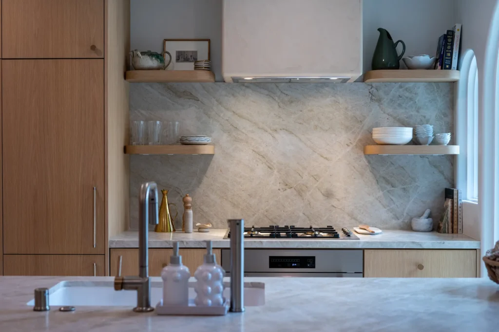 A kitchen stove area with a sleek white range hood flanked by two small wood floating shelves.